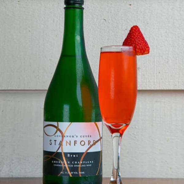 A green bottle of Stanford Brut champagne next to a flute of red mimosa garnished with a strawberry.