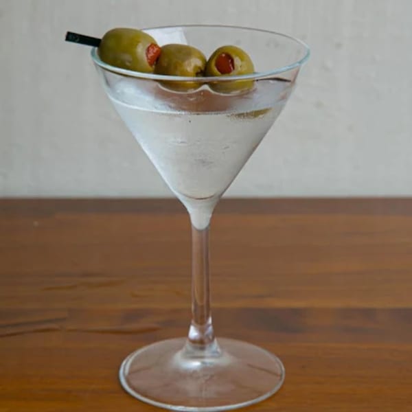 A martini glass filled with a clear drink and three green olives on a pick.