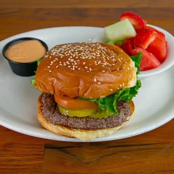 A hamburger with lettuce, tomato, and pickles, served with a side of fruit and dipping sauce.