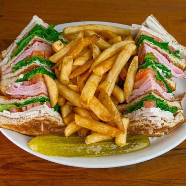 A club sandwich with fries and a pickle spear on a white plate at Park Pantry.