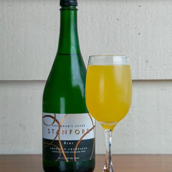 A green bottle of Stanford Brut champagne next to a glass of mimosa.