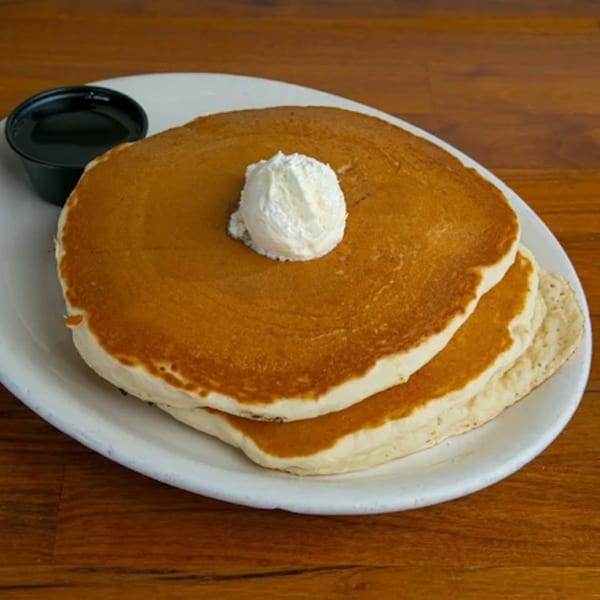 Stack of golden pancakes topped with a dollop of whipped butter and a side of syrup.