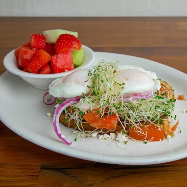 Poached eggs on toast with tomatoes, red onion, sprouts, feta, and a side of fruit.