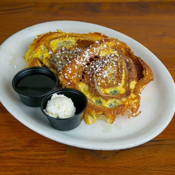 Cinnamon roll French toast with powdered sugar, syrup, and whipped butter on a white plate.